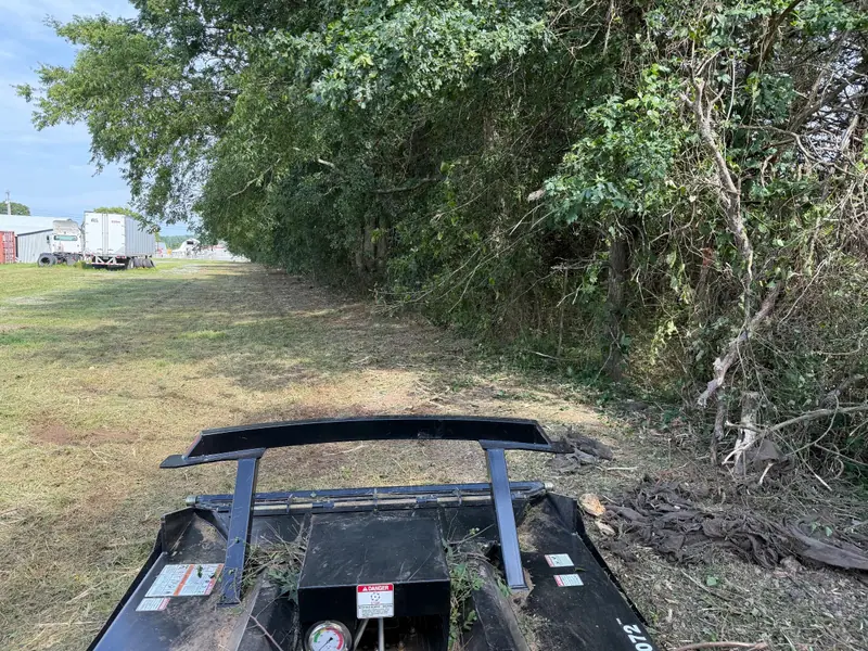 Brush cutter attachment in front of a cleared fence line