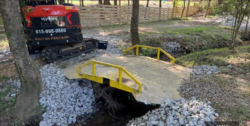 Compact excavator with Precision Siteworks lettering setting rock around a creek bridge