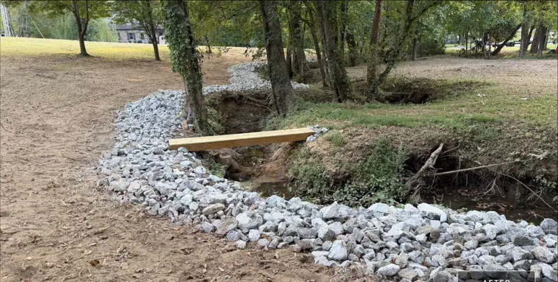 Creek bank lined with new rock beside a freshly graded slope under trees