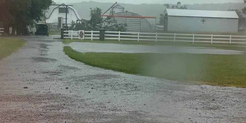 Front yard flooded in a heavy rain, water pooled between the gravel drive and a white board fence