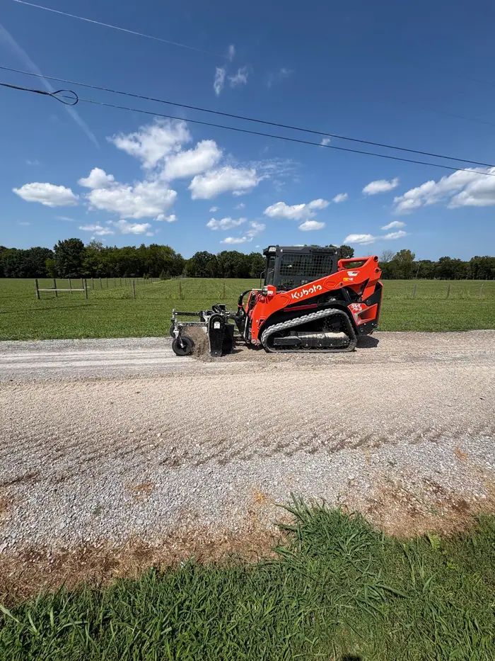 Tracked loader with a power rake working a gravel driveway