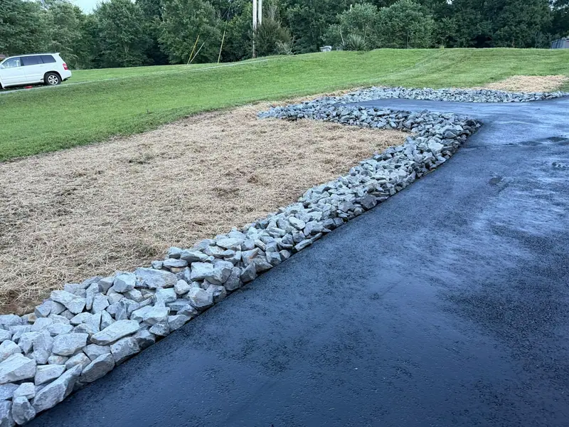 Driveway edge lined with rock beside a freshly seeded slope