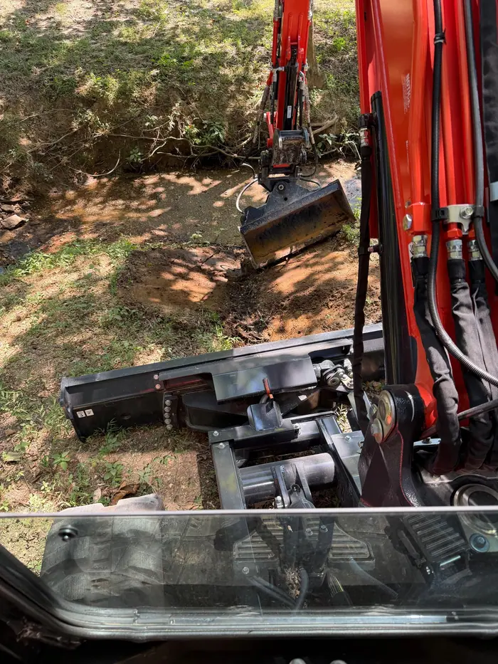 Operator’s view from the cab of a compact excavator digging along a creek bank