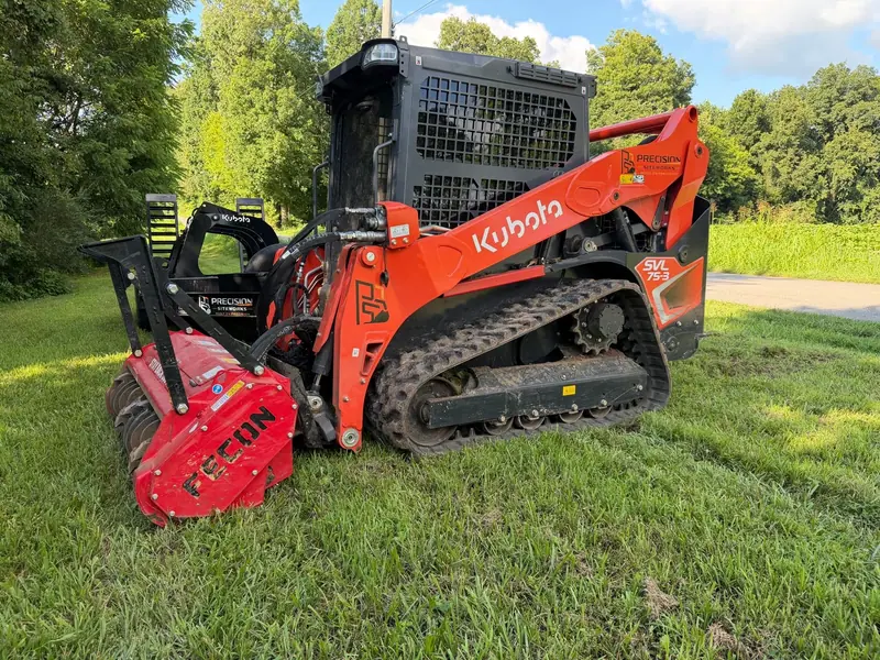 Orange Kubota tracked loader fitted with a red forestry mulching head, parked on grass
