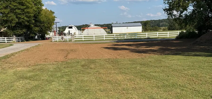 Freshly graded yard beside a white board fence with barns behind