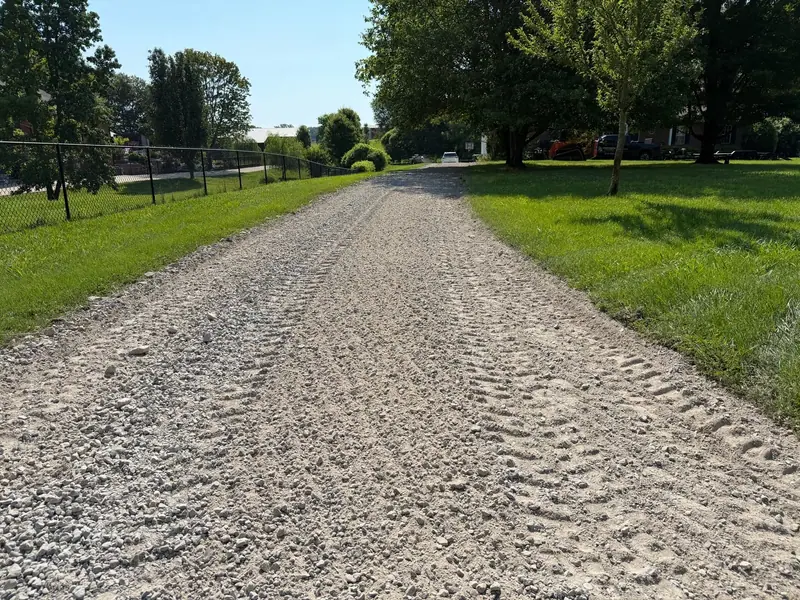Long regraded gravel driveway between a fence and mowed grass