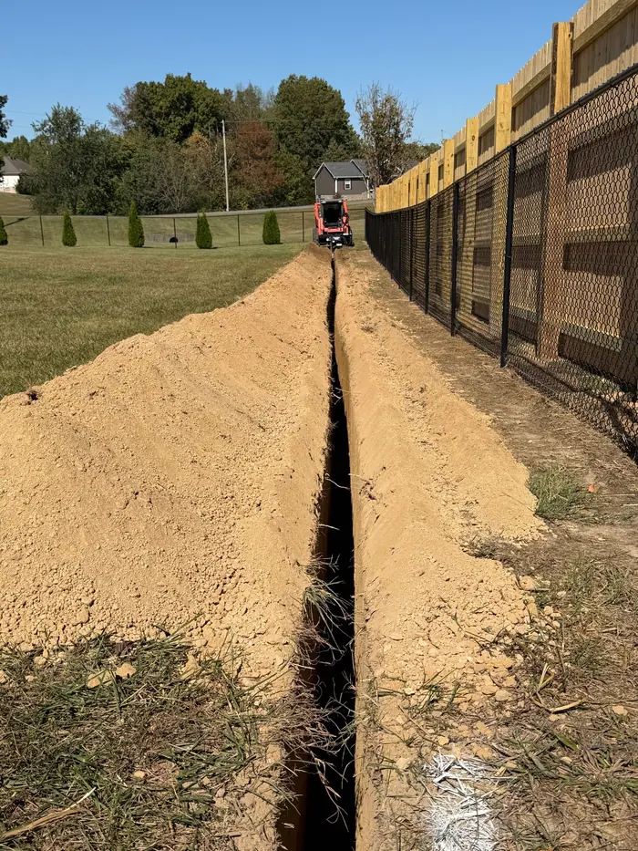 Long, narrow trench cut in a straight line along a wooden privacy fence