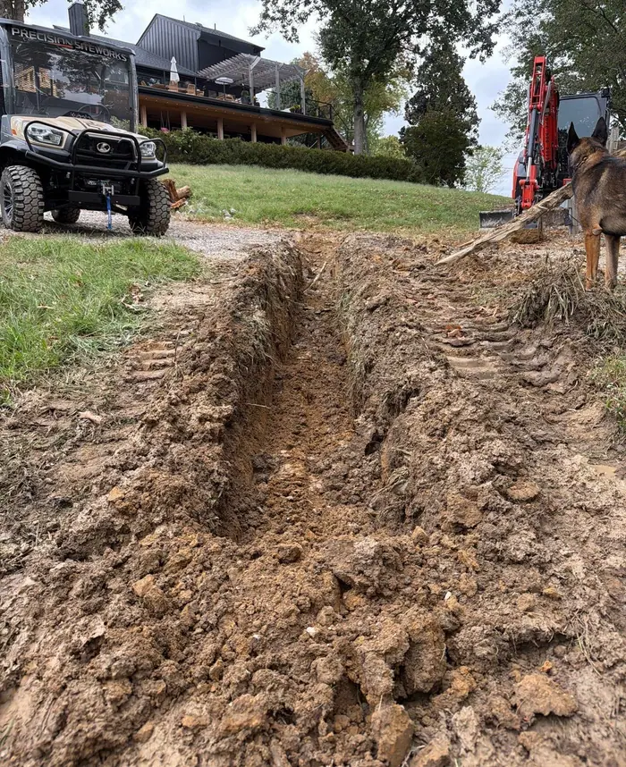 Freshly dug trench running across a yard toward a house, utility vehicle parked nearby