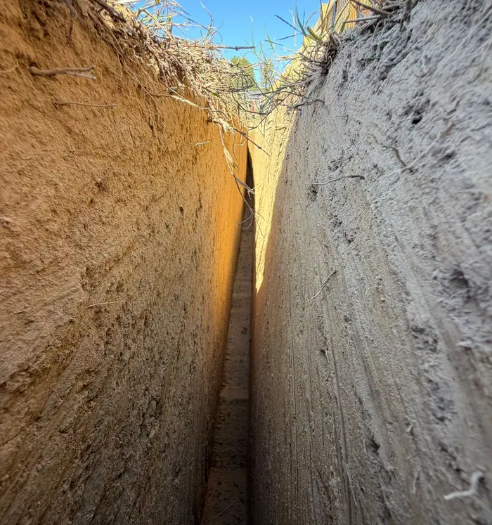 Looking down into a narrow trench with clean clay walls